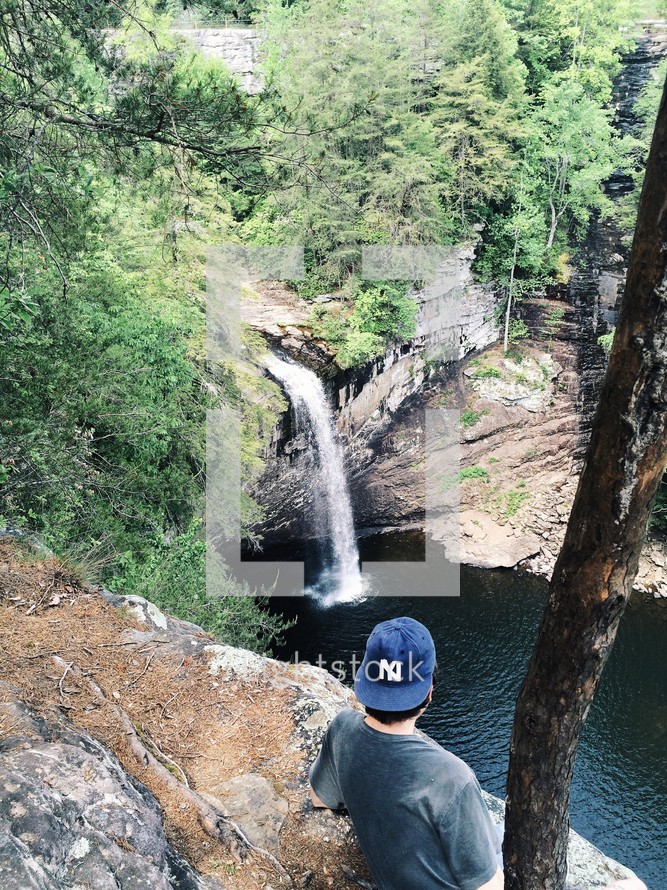 man standing at the edge of a cliff looking down at a waterfall 