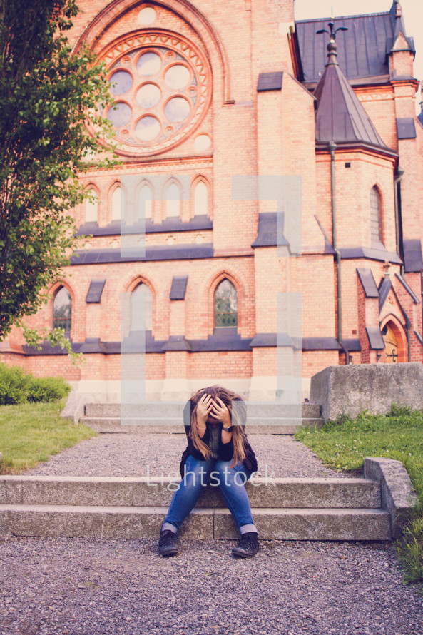 woman with her head down sitting in front of a church 