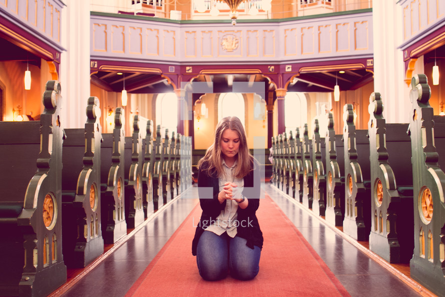 woman kneeling in prayer in an aisle of a church 
