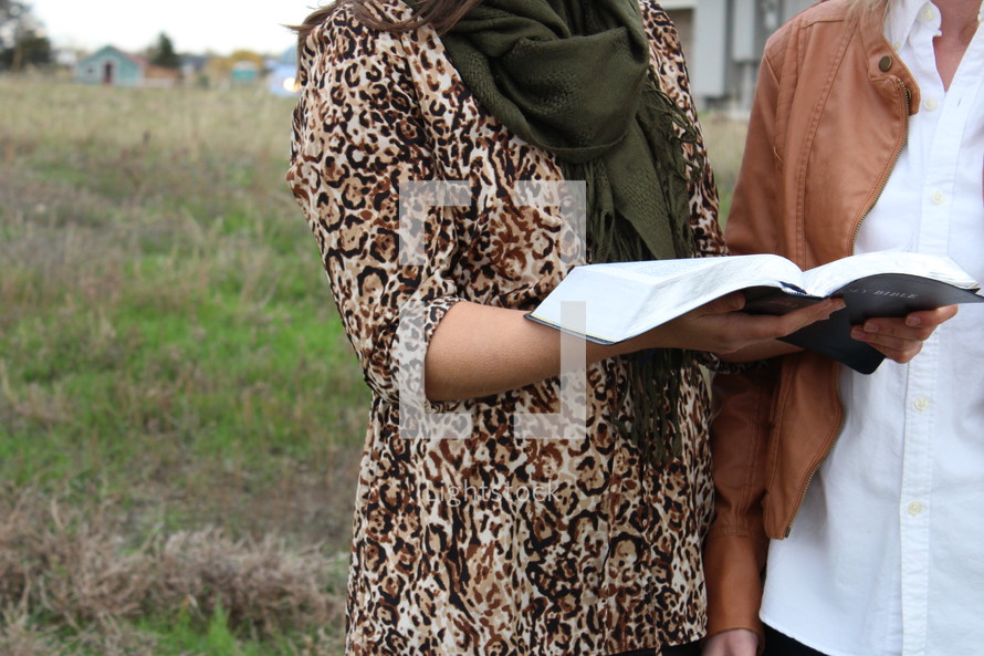 women standing outdoors reading a Bible 