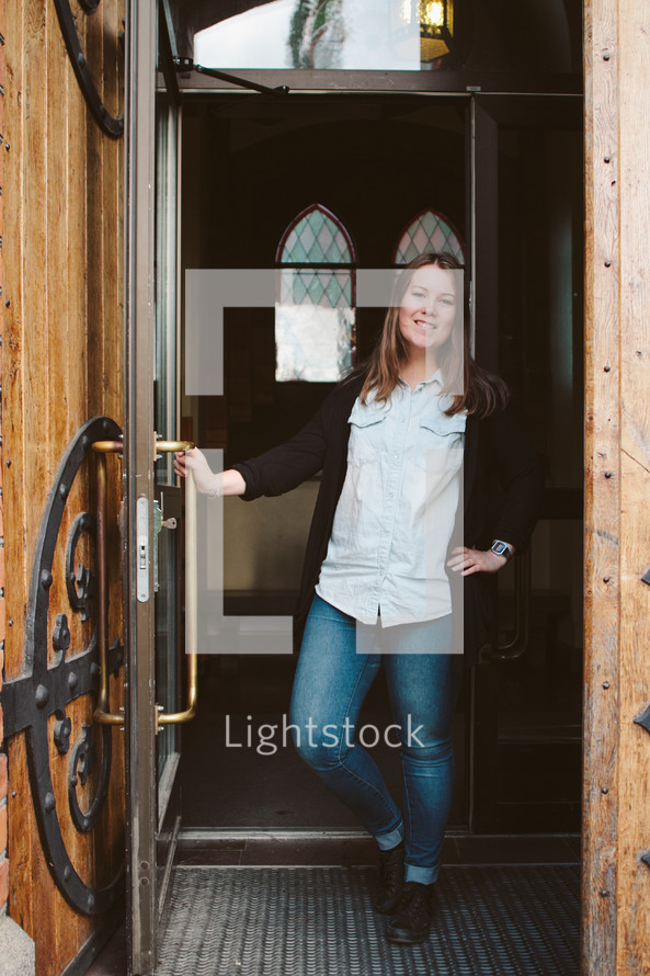 Woman standing in a doorway entrance holding the door.