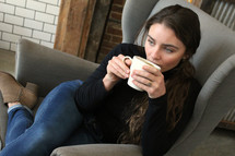 a woman sitting in a chair drinking coffee 