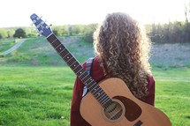 a woman standing outdoors with a guitar on her back 
