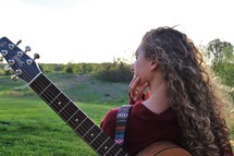 a girl standing outdoors with a guitar on her back 