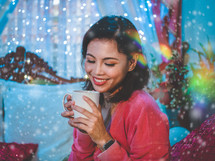 a smiling woman holding a mug surrounded by bokeh lights 