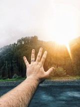 a man's hand raised towards a sunburst 