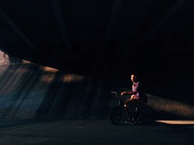 Man riding a bike under a bridge.