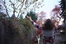 a woman in a coat outdoors with raised hands in fall 