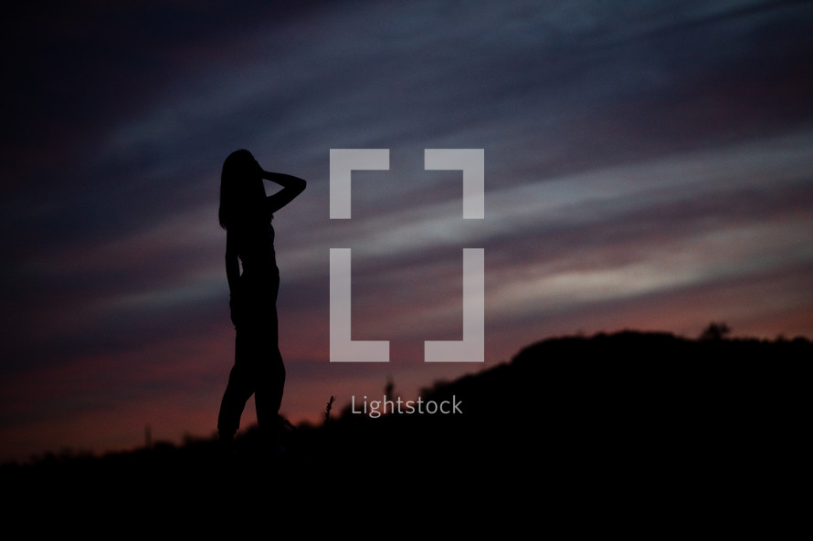 silhouettes of a young woman on a mountaintop at sunset 