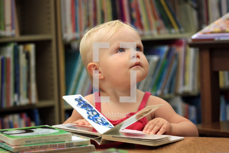 a toddler girl reading a book in a library 