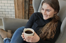 a woman sitting in a chair holding a cup of coffee 