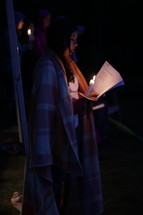 a woman in a blanket holding a candle and sheet music 