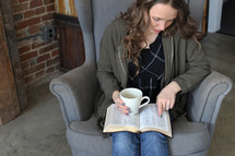 a woman reading a Bible in her lap while holding a coffee mug 