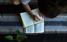 a girl reading a Bible and writing in a notebook 