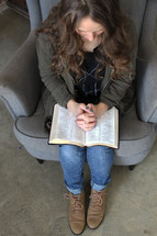 a woman praying over a Bible in her lap 