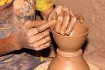 Hands molding clay on a potter's wheel.