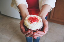 A woman holding out a cupcake.