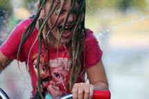 a girl child riding her bike through a sprinkler 