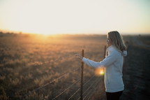 a woman looking out into a field at sunset 