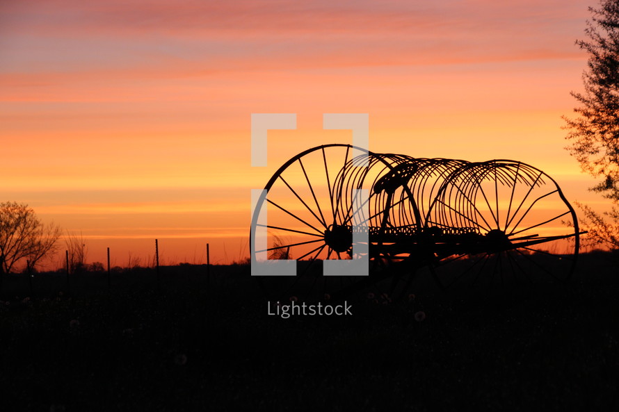 silhouette of a hay baler at sunrise