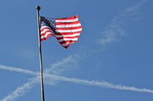 American flag on a flag pole with airplane vapor trails in the sky in the shape of a cross