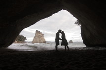 Silhouette of a couple kissing in a cave on the beach.