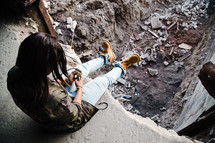 a person sitting at the edge of a hole in a building looking at their cellphone 