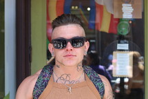 man with sunglasses, tattoos, ear gauges, and a backpack 