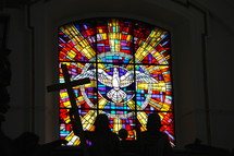 Stained glass window depicting the Holy Spirit descending like a dove with silhouette of man holding christian cross