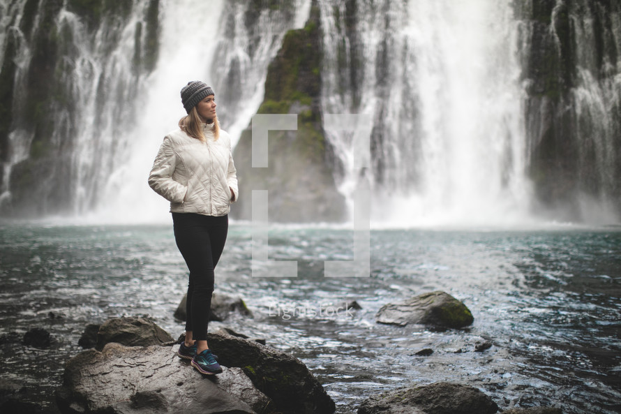 woman in a coat and waterfall in the background 