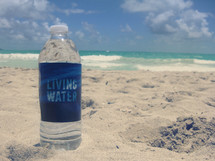 living water bottle on the sand of a beach 