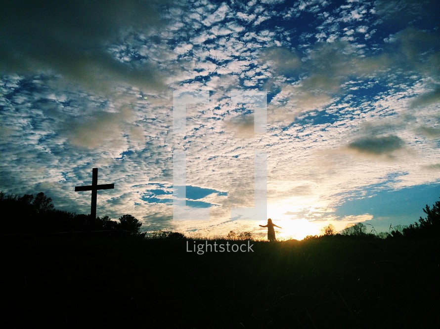 cross under a cloudy sky and silhouette of a girl child 