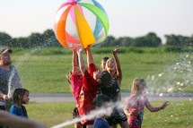 children playing outdoors with beach balls and water hoses 