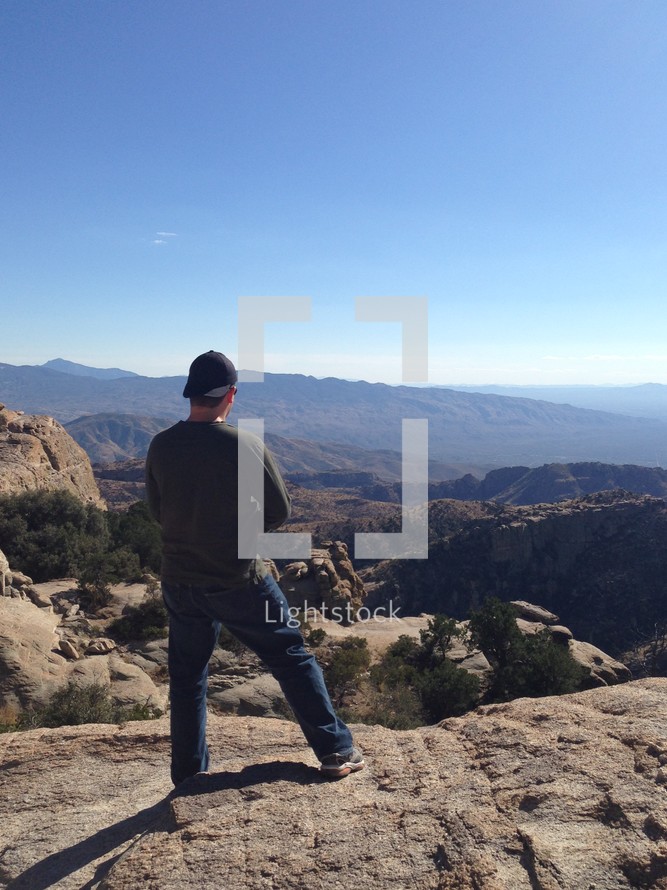 a man standing on a desert mountain taking in the view 