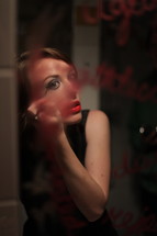 Woman putting on makeup in a lipstick-covered mirror.