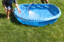 children filling a plastic swimming pool with water 