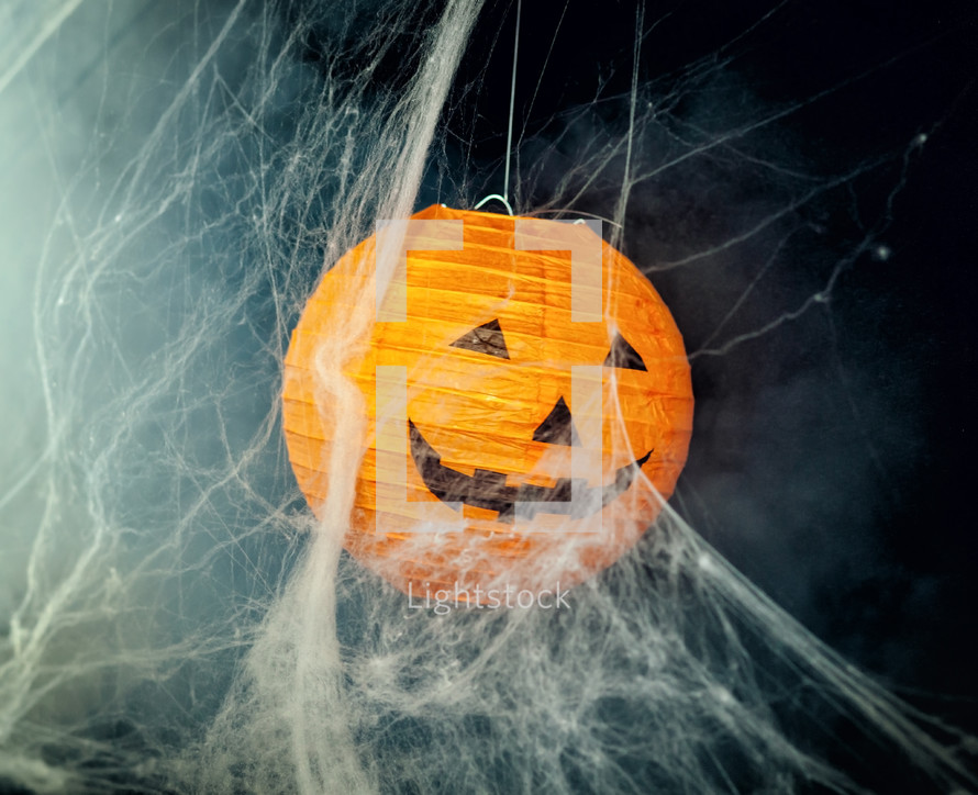 Pumpkin among cobwebs and fog on black background. Halloween image.