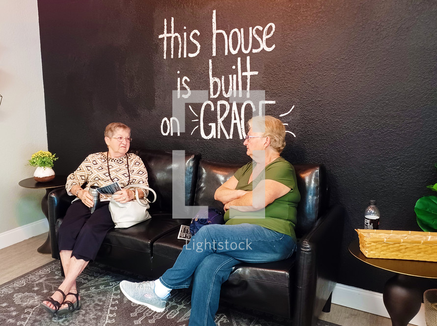 Two women chatting in front of "This house is built on Grace" mural
