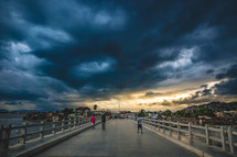 pedestrians walking on an island bridge under a cloudy sky 