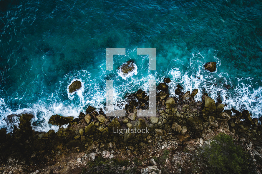 aerial view over waves crashing into a rocky shore 