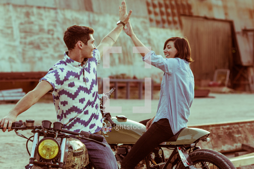 a man and woman on motorcycles giving each other a high five 