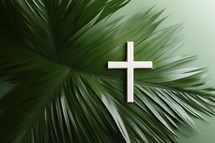Wooden christian cross on green palm leaf background, top view