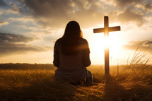 Silhouette of woman praying with cross at sunset