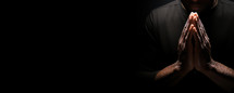 Praying man in black cloth on black background with copy space