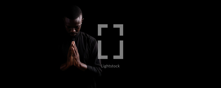 Black man praying on black background with copy space. Praying concept