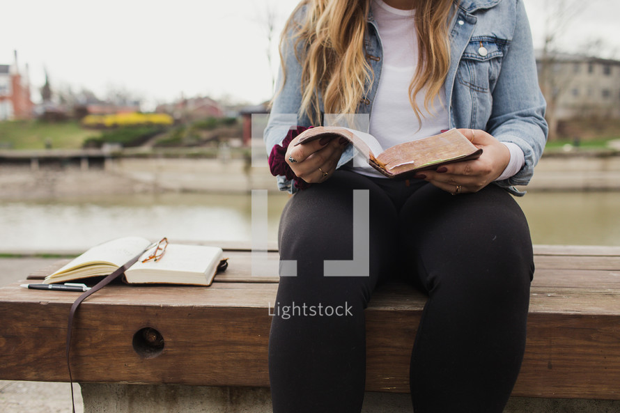 a young woman sitting on a bench reading a Bible 