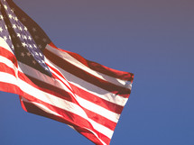 An American flag fluttering against a blue sky.
