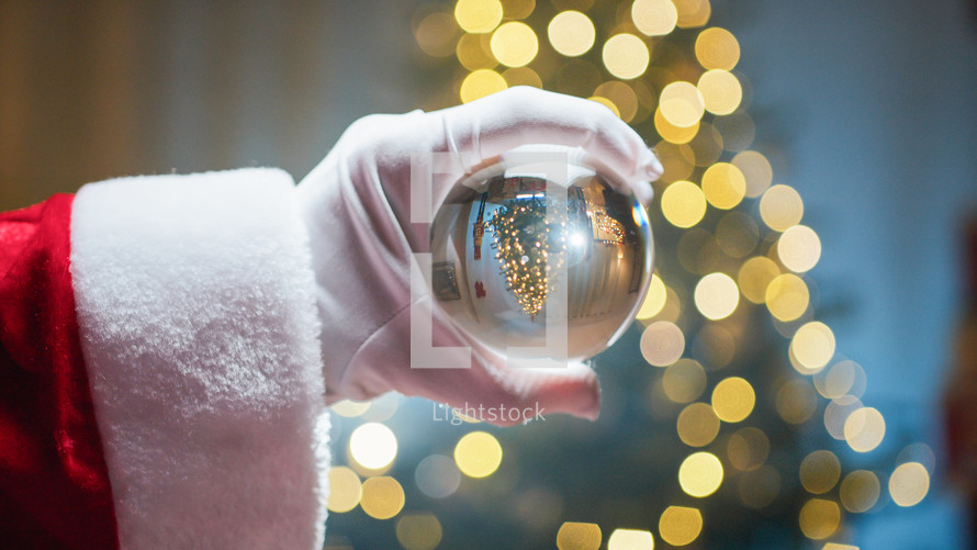 Santa Holding Magic Glass Ball Against Christmas tree