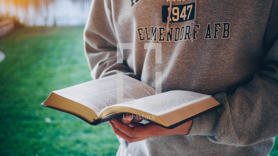 teen boy in a sweatshirt reading a Bible 