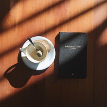 empty cup and productivity planner book in sunlight and shadows on a table 